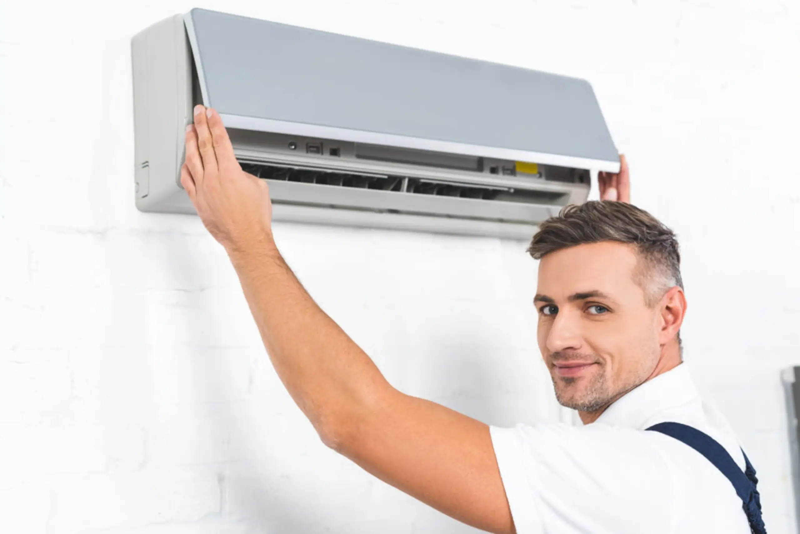 A technician installing or repairing an air conditioner unit mounted on a white wall, showcasing the open panel and internal components.